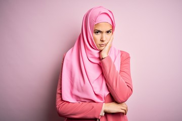 Poster - Young beautiful girl wearing muslim hijab standing over isolated pink background thinking looking tired and bored with depression problems with crossed arms.