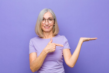 Wall Mural - senior or middle age pretty woman smiling, feeling happy, carefree and satisfied, pointing to concept or idea on copy space on the side