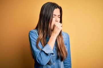 Poster - Young beautiful girl wearing casual denim shirt standing over isolated yellow background feeling unwell and coughing as symptom for cold or bronchitis. Health care concept.