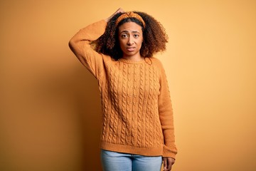 Young african american woman with afro hair wearing casual sweater over yellow background confuse and wonder about question. Uncertain with doubt, thinking with hand on head. Pensive concept.