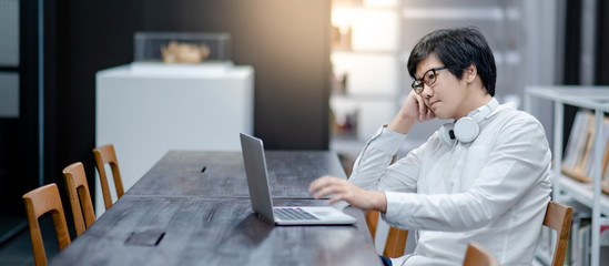 Asian man entrepreneur wearing glasses and headphones using laptop at home office. Businessman working with personal computer thinking about business project. Work smart with modern technology.