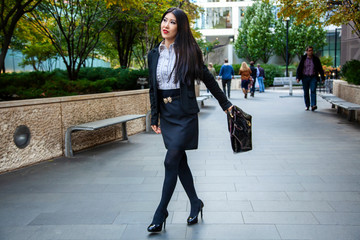 Beautiful Chinese Asian woman in fashionable business attire is enjoying a nice day walking around downtown Chicago in the afternoon.  She carries a trendy handbag and black blazer with red lipstick