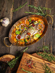 Wall Mural - Top view on a delicious dish of home-made seabass fillet with mushrooms and potatoes in a saucepan in a pan on a wooden table, vertical format