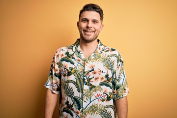 Wall Mural - Young man with blue eyes on vacation wearing floral summer shirt over yellow background with a happy and cool smile on face. Lucky person.