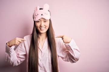 Sticker - Young asian woman wearing pajama and sleep mask over pink isolated background looking confident with smile on face, pointing oneself with fingers proud and happy.