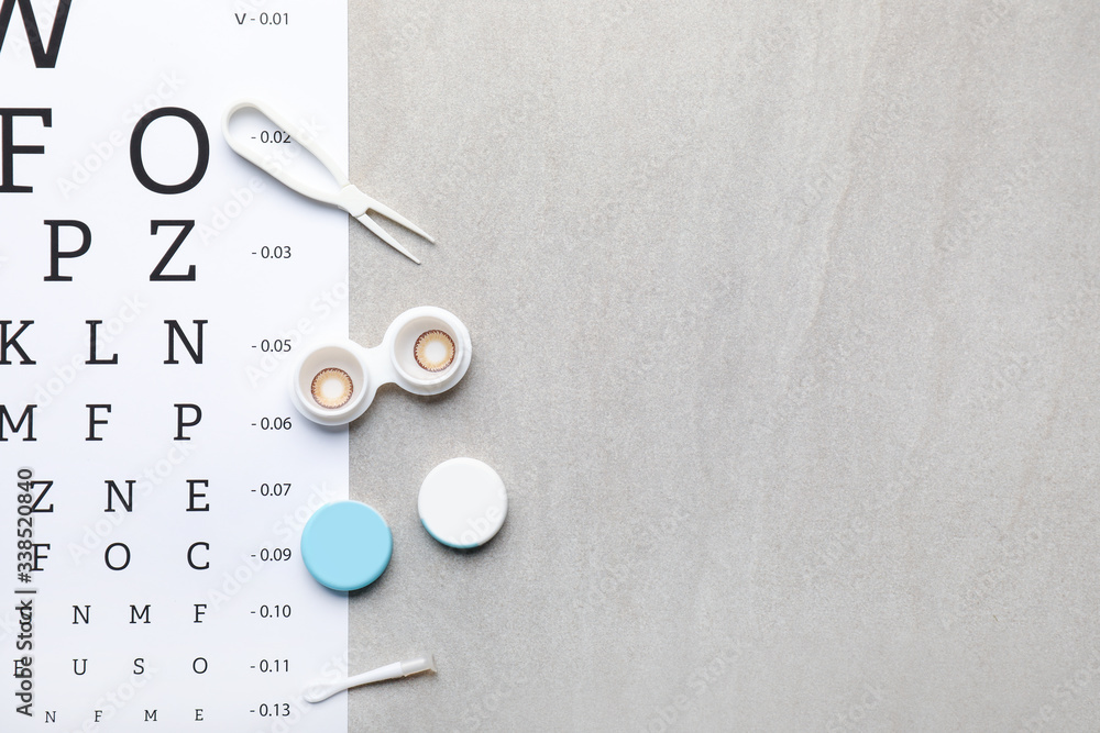 Container with contact lenses, tweezers and eye test chart on grey background