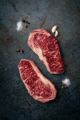 Wall Mural - Two raw, fresh Wagyu marbled beef steaks, strip loin on a dark stone background, top view