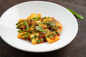 Wall Mural - Cooked ravioli with tomatoes, pesto sauce and Basil leaves on a white plate, close-up