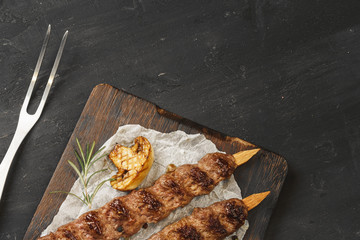 Wall Mural - Grilled Lula kebab on skewers served on wooden board, black table background