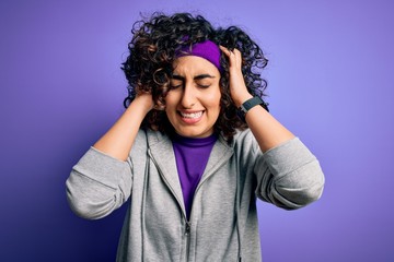 Sticker - Beautiful curly arab sportswoman doing sport wearing sportswear over purple background suffering from headache desperate and stressed because pain and migraine. Hands on head.