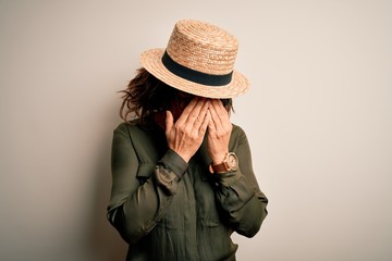 Canvas Print - Middle age brunette woman wearing glasses and hat standing over isolated white background with sad expression covering face with hands while crying. Depression concept.