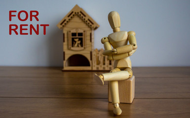 Wooden model of a sitting man in front of a miniature house. For rent inscription.