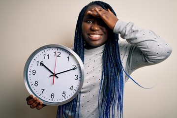 Poster - Young african american plus size woman with braids doing countdown holding big clock stressed with hand on head, shocked with shame and surprise face, angry and frustrated. Fear and upset for mistake.