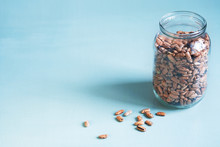 Pinto Beans In A Glass Jar With Grains On The Table On A Light Background With Empty Space On The Left. Minimalist Style Shot