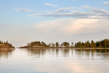 Summer. Evening.Calm Water Surface Of The Lake. In The Distance You Can See A Narrow Strip Of Rocky Shore,overgrown With Moss And Trees.On The Left Is The Passage Between The Islands. Gentle Blue Sky.