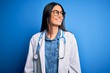 © Krakenimages.com - Young beautiful doctor woman wearing stethoscope and glasses over blue background looking away to side with smile on face, natural expression. Laughing confident.
