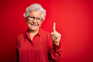 senior beautiful grey-haired woman wearing casual shirt and glasses over red background showing and 