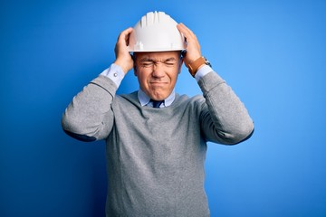 Poster - Middle age handsome grey-haired engineer man wearing safety helmet over blue background suffering from headache desperate and stressed because pain and migraine. Hands on head.