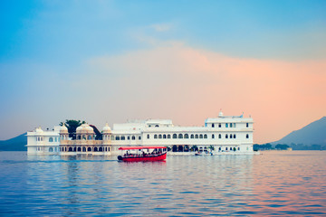 Fototapete - Romantic luxury India travel tourism - tourist boat in front of Lake Palace (Jag Niwas) complex on Lake Pichola on sunset with dramatic sky, Udaipur, Rajasthan, India