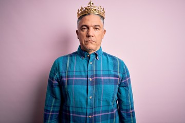 Poster - Middle age handsome grey-haired man wearing golden crown of king over pink background with serious expression on face. Simple and natural looking at the camera.