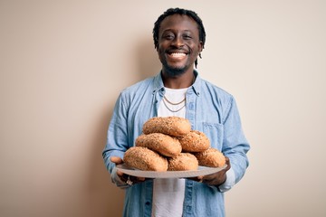 Sticker - Young african american man holding tray with healthy wholemeal bread over white background with a happy face standing and smiling with a confident smile showing teeth