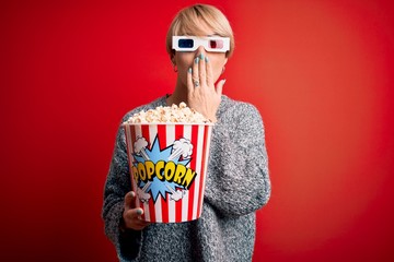 Wall Mural - Young blonde woman with short hair wearing 3d movie glasses and eating popcorn at the cinema cover mouth with hand shocked with shame for mistake, expression of fear, scared in silence, secret concept