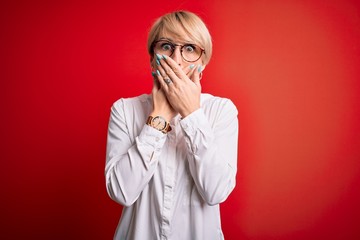 Sticker - Young blonde business woman with short hair wearing glasses over red background shocked covering mouth with hands for mistake. Secret concept.