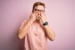 Young handsome redhead man wearing casual t-shirt standing over isolated pink background rubbing eyes for fatigue and headache, sleepy and tired expression. Vision problem