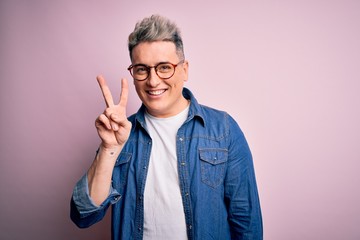 Young handsome modern man wearing glasses and denim jacket over pink isolated background showing and pointing up with fingers number two while smiling confident and happy.