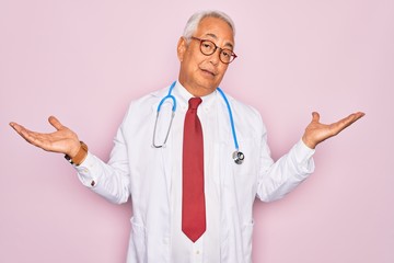 Sticker - Middle age senior grey-haired doctor man wearing stethoscope and professional medical coat clueless and confused expression with arms and hands raised. Doubt concept.