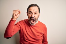 Middle Age Hoary Man Wearing Casual Orange Sweater Standing Over Isolated White Background Angry And Mad Raising Fist Frustrated And Furious While Shouting With Anger. Rage And Aggressive Concept.