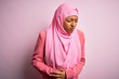 © Krakenimages.com - Young African American afro woman wearing muslim hijab over isolated pink background with hand on stomach because indigestion, painful illness feeling unwell. Ache concept.