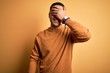 © Krakenimages.com - Young brazilian man wearing casual sweater standing over isolated yellow background smiling and laughing with hand on face covering eyes for surprise. Blind concept.