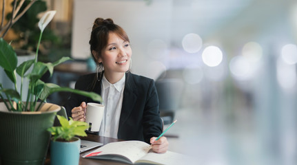 Young woman asian with laptop online learning. Lifestyle social distance education. Development skills by yourself. Lady asian in workplace office modern business. Green corporate environment.