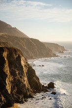 Aerial Drone View Of The Big Sur Coastline In California. Beautiful Golden Light Hitting The Side Of The Cliffs At Sunset Along The Coastal Road.