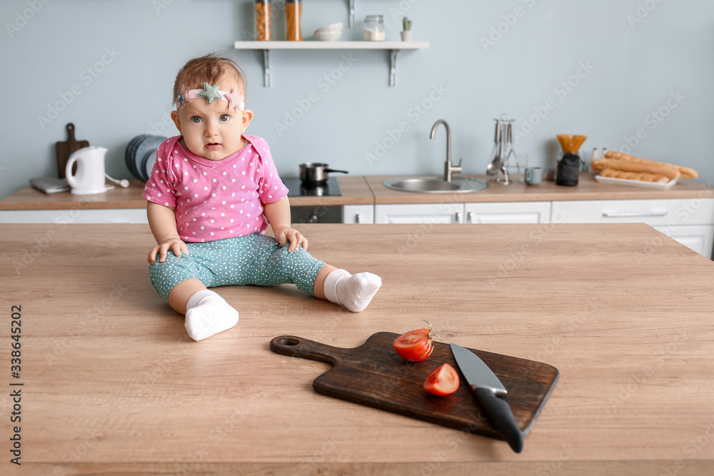 Little baby playing with cutting board and knife in kitchen. Child in danger