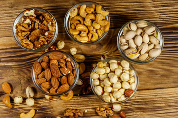 Poster - Assortment of nuts on wooden table. Almond, hazelnut, pistachio, walnut and cashew in glass bowls. Top view. Healthy eating concept