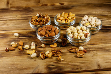 Poster - Assortment of nuts on wooden table. Almond, hazelnut, pistachio, walnut and cashew in glass bowls. Healthy eating concept