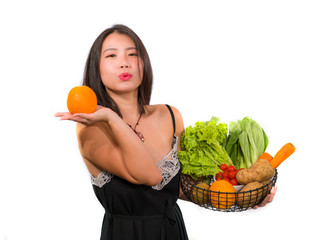 young happy and beautiful Asian Chinese woman holding basket full of vegetables smiling cheerful holding orange playful in healthy organic and natural nutrition