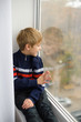 © cheese78 - boy sits on windowsill, near window glass, wants to walk on street, but in world there is coronavirus pandemic, and he remains at home