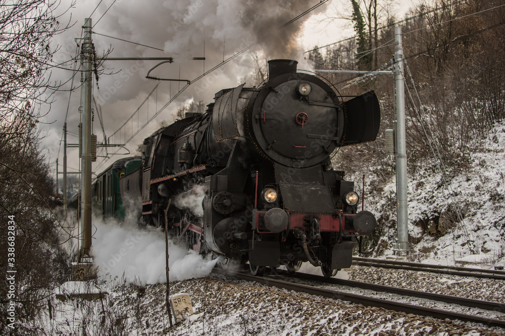 Front of the european style war train steam locomotive. German war locomotive built during the second world war rushing on the snowy train track, letting out steam and smoke.