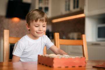 Wall Mural - A boy in the kitchen sits and smiles, in front of him is a box of delicious dried fruits