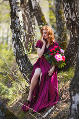 Wall Mural - red-haired girl in a burgundy dress walks in the forest