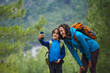 © zhukovvvlad - A child with a backpack takes a selfie on a smartphone with mom on the background of a mountain forest.