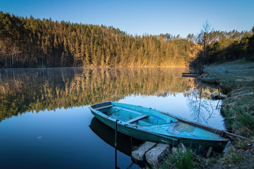  Mirroring forest on pond surface and blue boat
