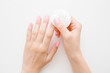 Young woman hand removing pink nail polish with white cotton pad on light gray table background. Point of view shot. Closeup. Top down view.
