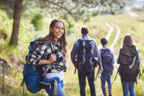 Girl with a backpack with friends, tourists walking in nature. Poster Mural XXL