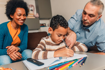 Parents helping their son with his homework at home in living room.