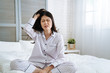 © PR Image Factory - frowning young girl feeling tired doesn't want wake up in the morning. unhappy lady with hand scratching hair with itch head. exhausted asian japanese woman mad sitting on bed in bright bedroom.