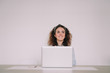 © NatRomero - A young brunette woman with curly hair is in front of her laptop. She is enjoying a cup of coffee with the mug between her hands. She is looking through the window screen with a happy gesture.